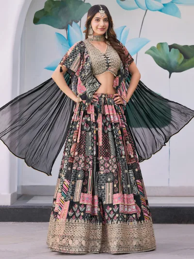 Woman wearing a black multicolor embroidered chinnon silk lehenga with cape sleeves and choker-style dupatta, perfect for weddings and festive occasions.