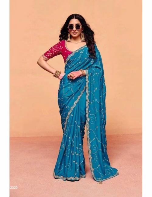 Model wearing a shimmering teal blue pure fancy tissue designer saree with scalloped embroidered borders and a contrast maroon handwork blouse.