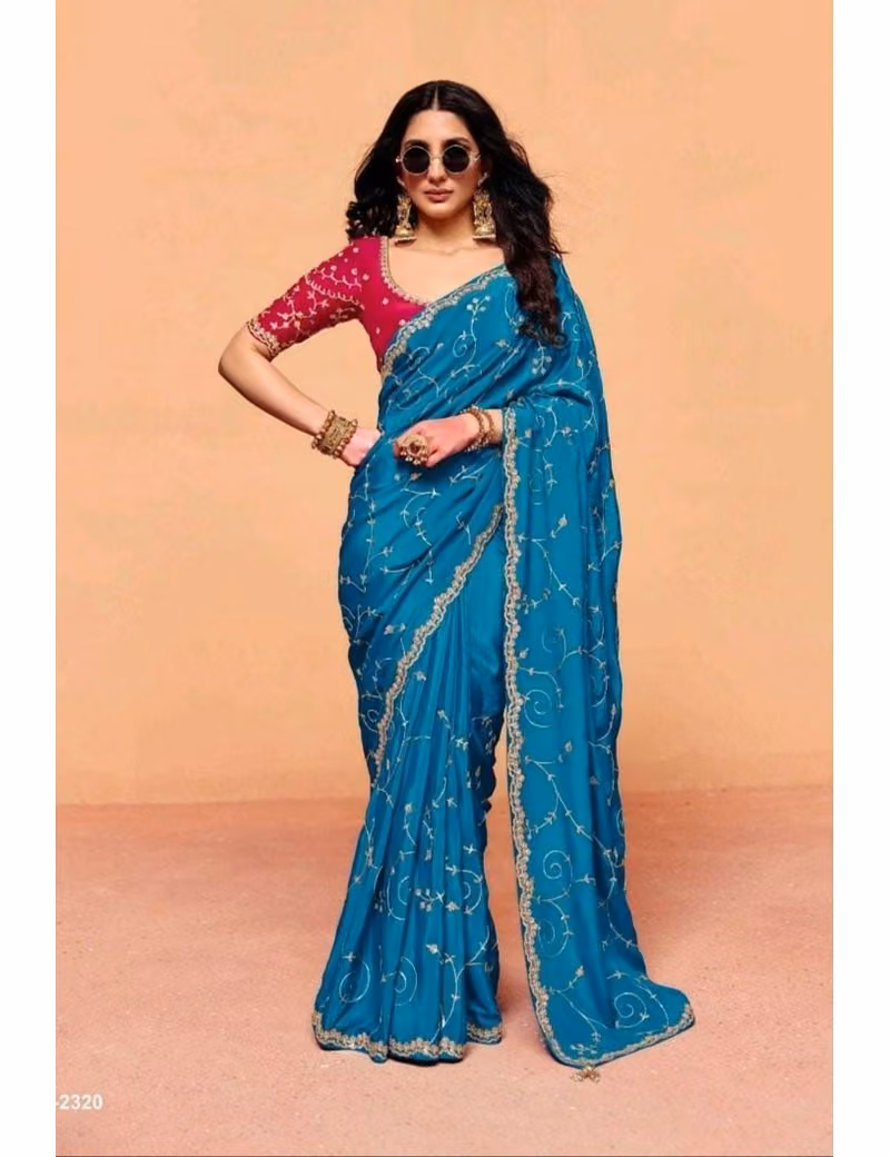 Model wearing a shimmering teal blue pure fancy tissue designer saree with scalloped embroidered borders and a contrast maroon handwork blouse.