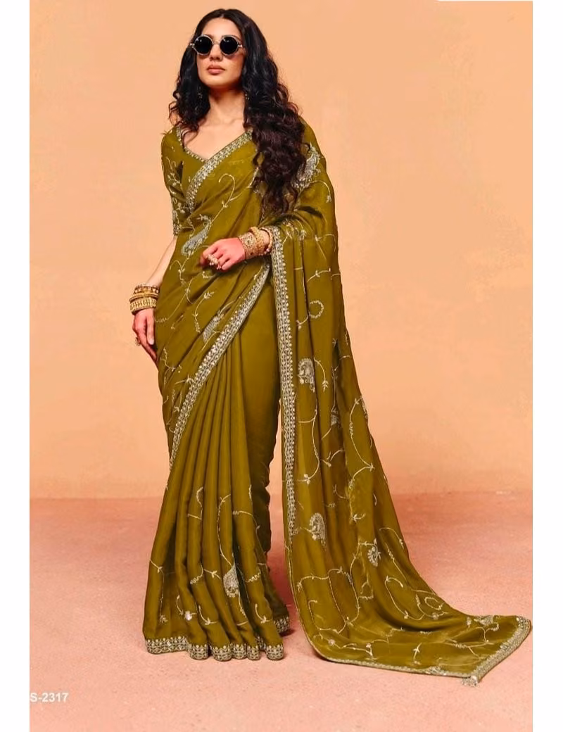 Model wearing a shimmering teal blue pure fancy tissue designer saree with scalloped embroidered borders and a contrast maroon handwork blouse.