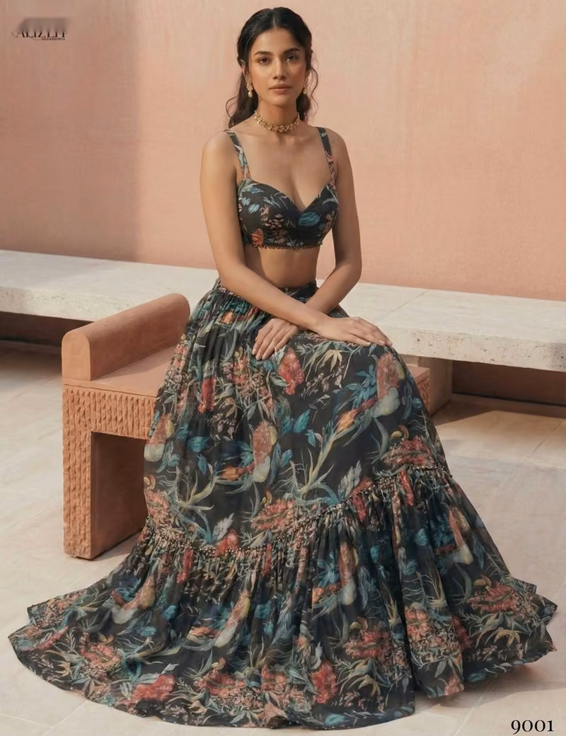 Model sitting on a stone bench wearing the Voguevive black floral print georgette lehenga, displaying the 4-meter skirt flare.
